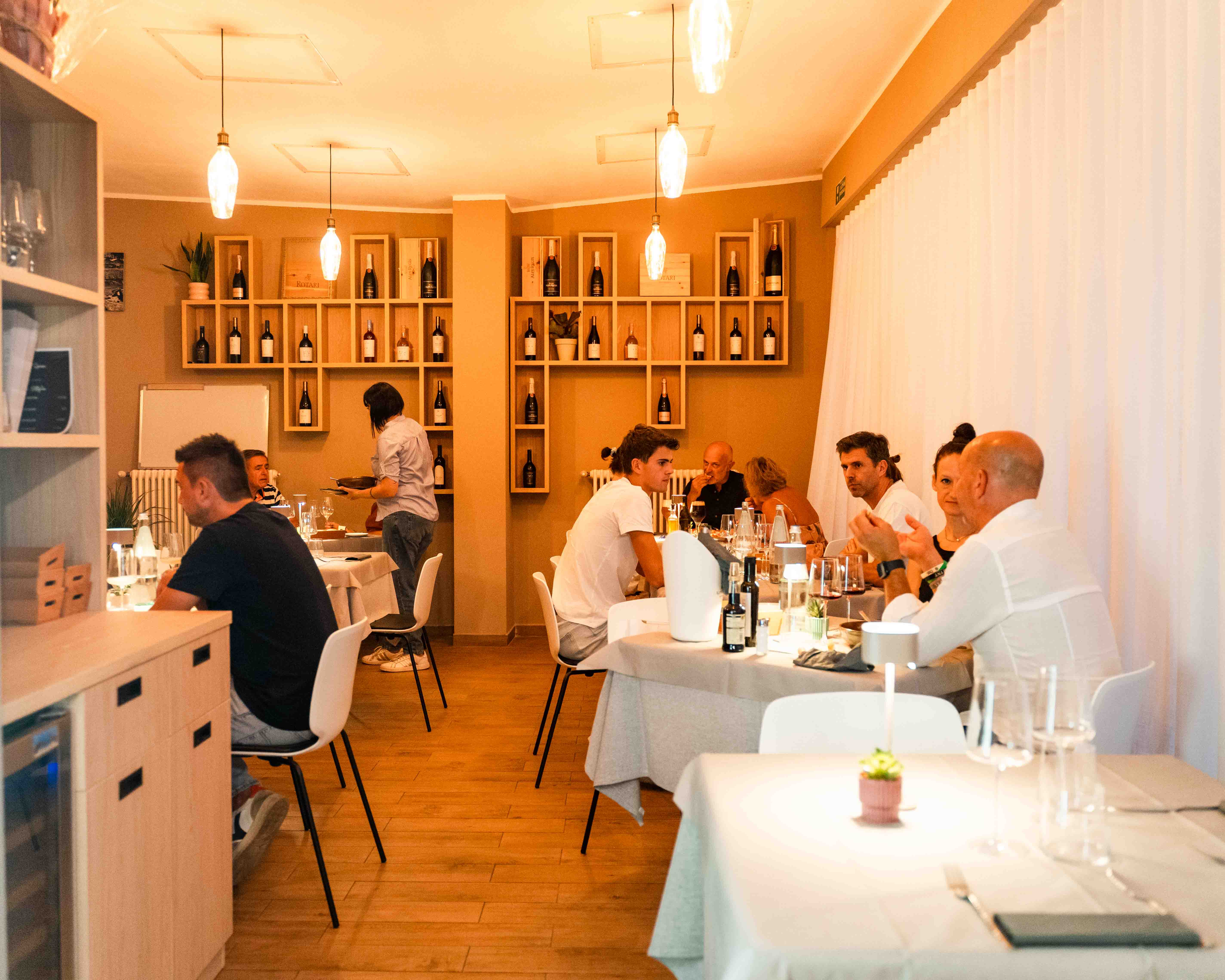 Sala del ristorante con tavoli occupati e parete vini